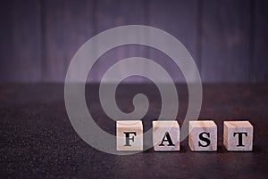 The word fast on wooden cubes, on a dark background, light wooden cubes signs, symbols signs