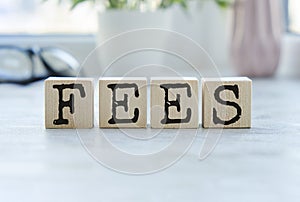 word FEES on wooden cubes on blue background. the inscription on the cubes is reflected from the surface. business