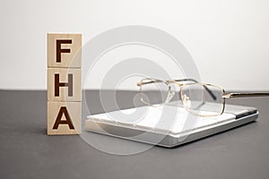 the word FHA is written on wooden cubes on a gray background. close-up of wooden elements, magnifying glass, paper documents and