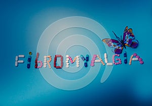 The word Fibromyalgia written by colorful medicines, pills, drugs, tablets, capsules with purple butterfly on a blue background