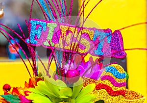The word `fiesta` written in colorful glitter letters with sombrero and paper flowers