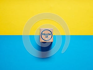 The word Follow Us on wooden cube button on blue and yellow background. Social media or internet followers concept