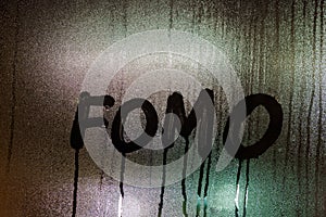 word FOMO - Fear Of Missing Out - handwritten on night wet window glass surface