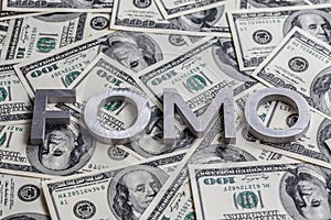 The word FOMO laid with aluminium letters on the US dollar banknotes background - with selective focus