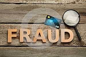 Word Fraud, credit card and magnifying glass on wooden background, flat lay