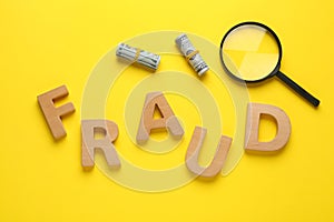 Word Fraud made of wooden letters, money and magnifying glass on yellow background, flat lay