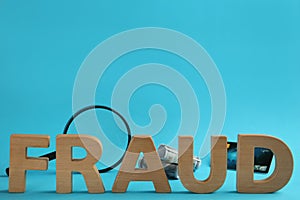 Word Fraud made of wooden letters near money, credit card and magnifying glass on light blue background, space for text