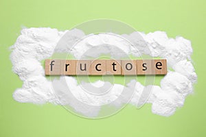 Word Fructose made of wooden cubes and powder on light green background, flat lay