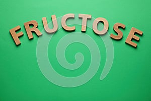 Word Fructose made of wooden letters on green background, flat lay. Space for text