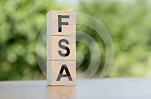 The word FSA - Flexible Spending Account, built from wooden cubes outdoors on the background of nature