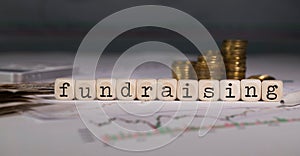 Word FUNDRAISING composed of wooden letter. Stacks of coins in the background