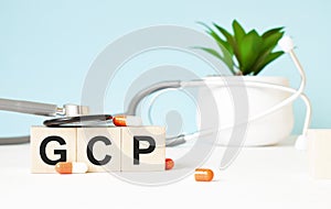 The word GCP is written on wooden cubes near a stethoscope on a wooden background. Medical concept