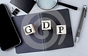 Word GDP on wooden block on black notebook with smartpone, credit card and magnifier