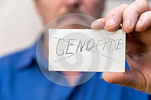 The word Genocide is crossed out. It is written in jagged gray letters on the paper. Man holding a white paper rectangle with