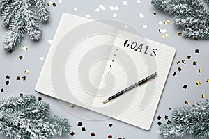 Word Goals written in notebook surrounded by Christmas decor on light grey background, flat lay