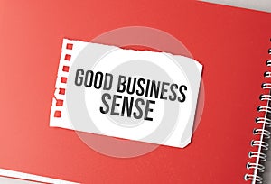 The word GOOD BUSINESS SENSE on torn paper on red notepad