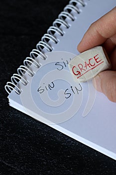 Word grace written on eraser in human hand placed over notebook page with handwritten word sin photo