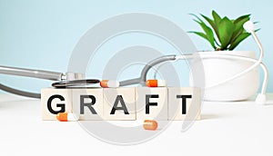 The word GRAFT is written on wooden cubes near a stethoscope on a wooden background. Medical concept