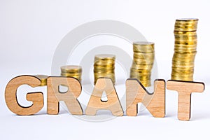 Word grant of three-dimensional letters is in foreground with growth columns of coins on blurred background. Monetary grant concep