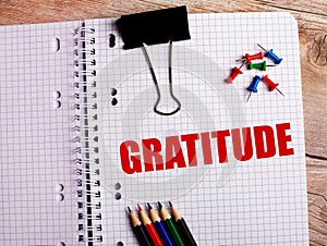 The word GRATITUDE is written in a notebook near multi-colored pencils and buttons on a wooden background