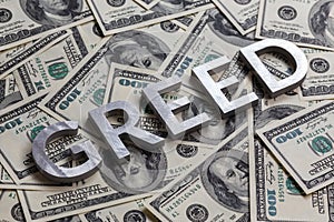 The word GREED laid with aluminium letters on the US dollar banknotes background - with selective focus photo