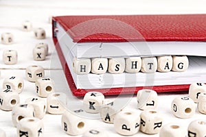 Word Hashtag written in wooden blocks in red notebook on white wooden table.