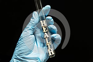 The word `health` in a glass test tube in the hands of a doctor in medical gloves on a black background, concept