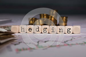 Word HEDGING composed of wooden letter. Stacks of coins in the background photo