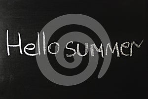 The word hello summer written in white chalk on a black chalkboard