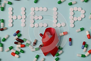 Word help is made of white pills against background of many multicolored capsules and a red ribbon
