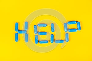 The word `Help` of tablets. Blue pills on yellow background word help. word help from tablets.