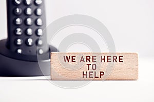 The word we are here to help on wooden block with telephone background. Business concept for customer support