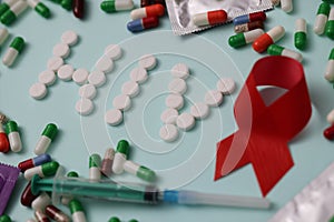 Word HIV is laid out from pills on background of multicolored capsules and singleuse syringe closeup