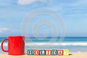 word HOLIDAY in colorful alphabet blocks and coffee cup on tropical beach