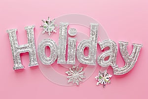 The word 'Holiday' dazzles in lustrous silver glitter against a soft pink backdrop