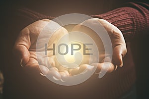 Word HOPE in abstract light in female hands, offering help, protection and support symbol. Sharing hope