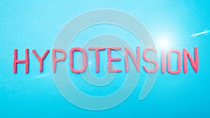 Word hypotension from red letters on a blue background. Arterial hypertension disease concept, medical, inscription