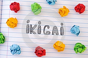 The word Ikigai on notebook sheet with some colorful crumpled paper balls around it photo