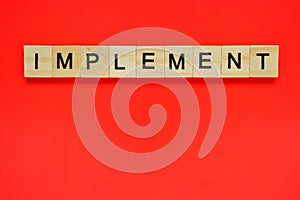 Word implement. Top view of wooden blocks with letters on red surface