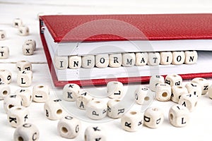 Word Information written in wooden blocks in red notebook on white wooden table.