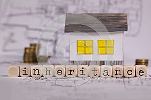 Word INHERITANCE composed of wooden letter. Small paper house in the background photo