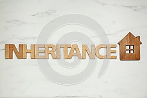 Word Inheritance made with wooden letters and house model on white marble background, flat lay