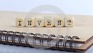 Word INVENT made with letters on wooden blocks on wooden notepad