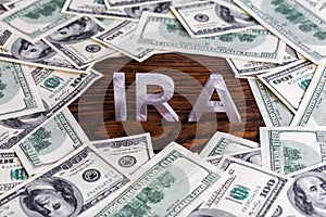 The word ira made of silver metal letters on wooden background surrounded by us dollar banknotes