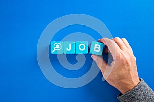 The word job on wooden cubes with on blue background. Searching for a job, employment, recruitment or career concept