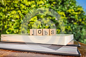 The word JOBS, letters cubes on books with green trees, nature background