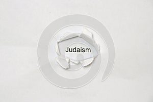 Word judaism on white isolated background through the wound hole in the paper.