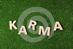 Word Karma made with wooden letters on green grass, top view