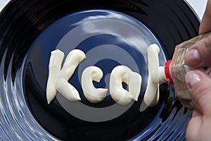 The word Kcal written by mayonnaise on a plate