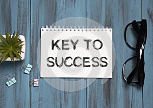the word Key To Success, is written in a notebook lying on white table with a pen, glasses and magnifier. Business
